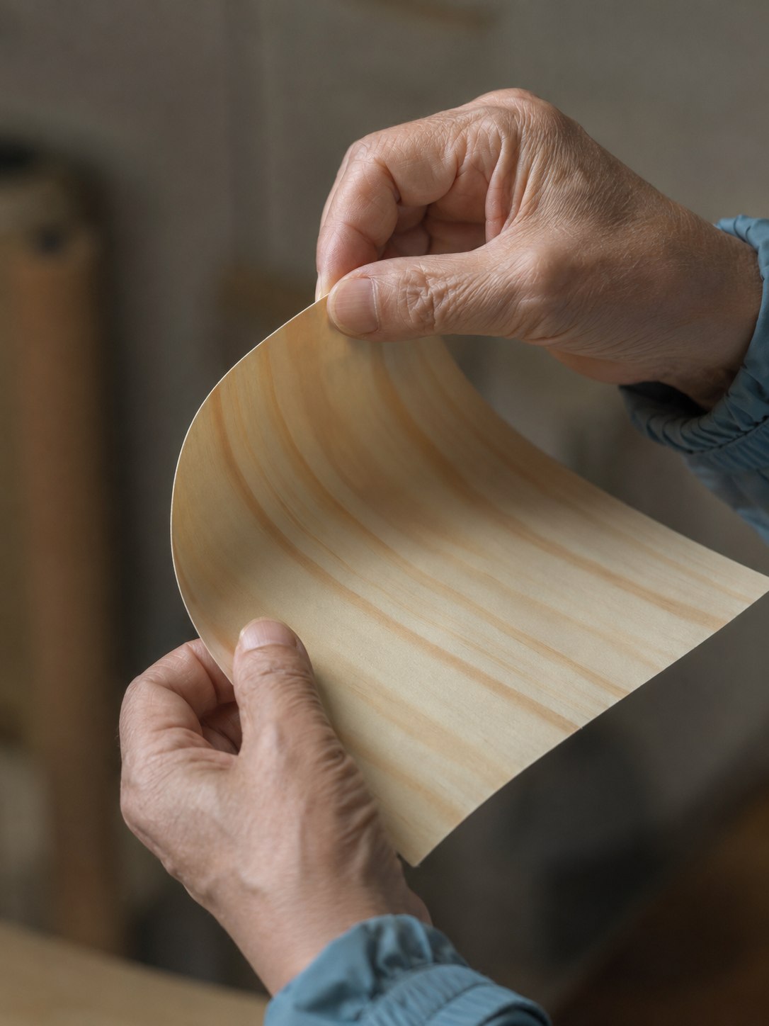 Hands gently bending a thin wood veneer sheet to show flexibility and grain